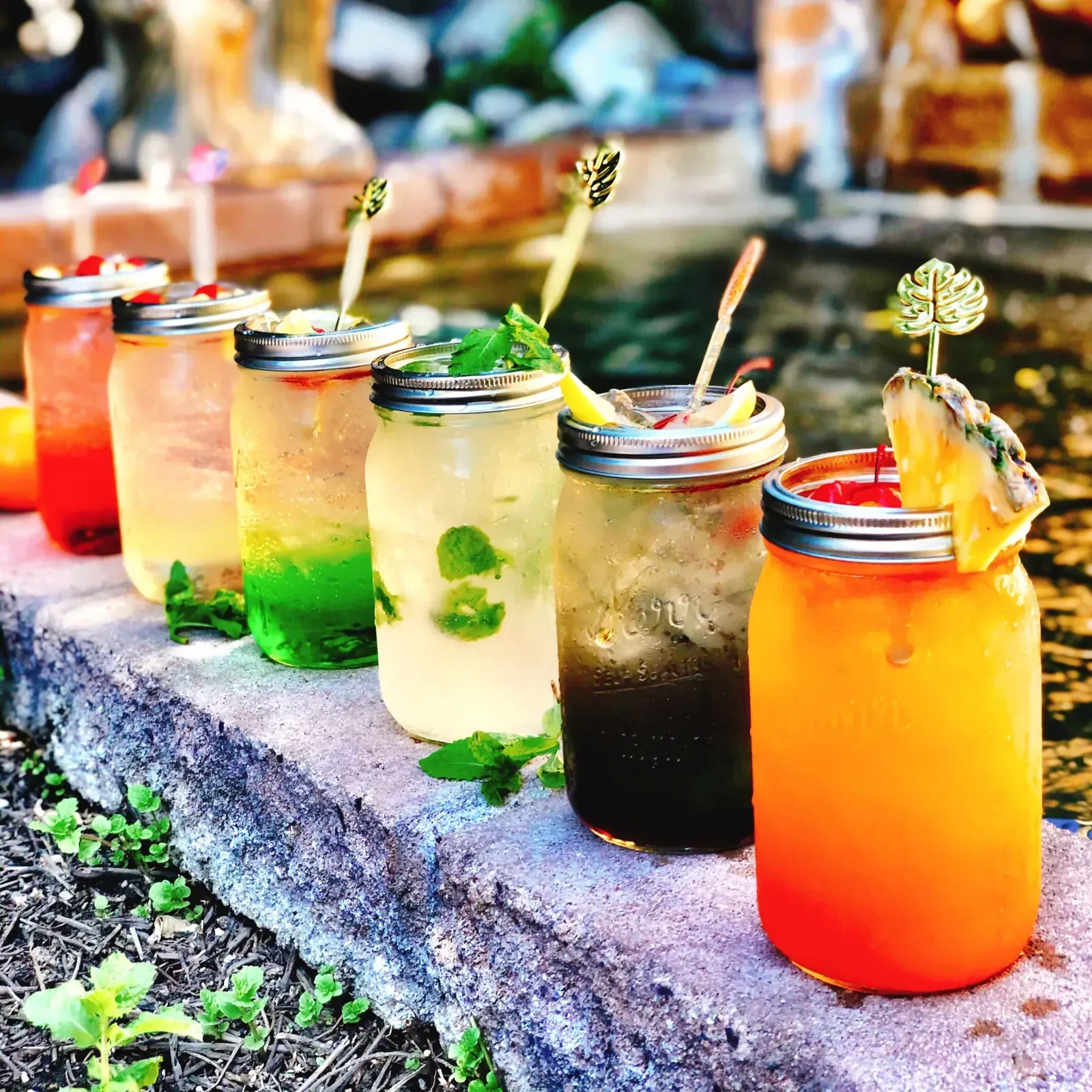 Row of colorful Thai House cocktails in mason jars garnished with mint and pineapple